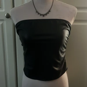 Svart tubtopp i syntetmaterial (skinn imitation)  - Snygg svart tubtopp. Perfekt för en stilren look. Enkel och elegant design som passar till många olika outfits. 