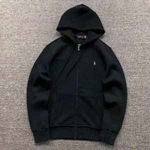 Svart hoodie från Ralph Lauren - Säljer en stilren svart hoodie från Ralph Lauren med dragkedja och broderad logga på bröstet. Tröjan har en klassisk design med huva och fickor framtill. Perfekt för en avslappnad look.