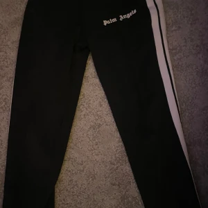 Svarta byxor från Palm Angels - Snygga svarta byxor från Palm Angels med vita sidoremsor och logga på höften. Perfekta för en stilren look. Byxorna har en normal passform och är tillverkade i ett bekvämt material.