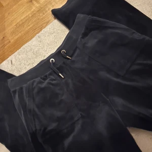  Juicy Couture byxor - Säljer ett par mörkblå mjukisbyxor från Juicy Couture. Byxorna har en bekväm passform med snörning i midjan och praktiska fickor med knappar. Perfekta för en avslappnad stil.