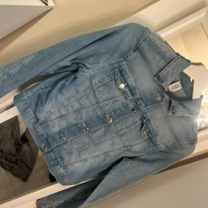Ljusblå jeansjacka från &Denim - Säljer en snygg ljusblå jeansjacka från &Denim. Jackan har en klassisk design med knappar framtill och två bröstfickor med lock. Perfekt för en avslappnad stil.