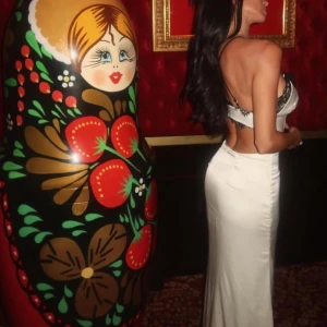 Vit långklänning med spetsdetaljer - Elegant vit långklänning med svarta spetsdetaljer och en djup v-ringning. Klänningen har en slits framtill och smala axelband. Perfekt för en sommarkväll vid stranden eller en festlig tillställning.