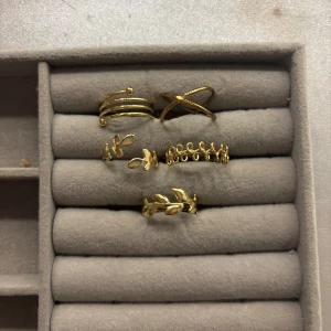 Set med guldiga ringar - Snyggt set med guldiga ringar i olika designer. Innehåller fem ringar med unika mönster, inklusive bladmotiv och korsad design. Perfekt för att mixa och matcha för en personlig stil.