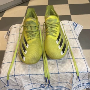 Gula fotbollsskor från Adidas Fluroskin - Säljer ett par gula fotbollsskor från Adidas med svarta och vita detaljer. Skorna har snörning och en modern design som passar perfekt för fotbollsplanen. De är lätta och bekväma, vilket ger bra kontroll och hastighet. + Har ett riktigt kolt lager med kolfiber på undersidan 