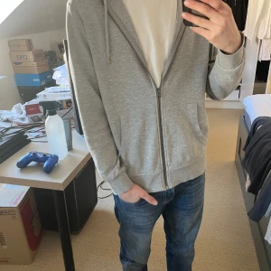 Grå zip hoodie  - En grå zip hoodie från jack&jones, använd fåtal gånger, är i storlek m själv är jag 171 cm och tycker den passar perfekt. Rekommenderar till en sen sommarkväll eller bara en vanlig dag i skolan 