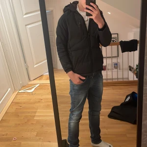 Svart pufferjacka från sail raicing - Säljer en svart pufferjacka från sail raicing med huva och dragkedjor på bröstet och sidorna. Jackan har en sportig look och är perfekt för kyliga dagar. Snygg och enkel design med diskret logga på bröstet. 7/10 skick.