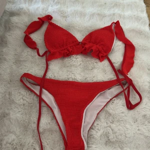 Röd bikini med knyt och ribbad struktur - Säljer en snygg röd bikini med ribbad struktur. Överdelen har trekantskupor och knytband i nacken och ryggen. Underdelen är högt skuren och har samma ribbade material. Perfekt för stranden eller poolen!