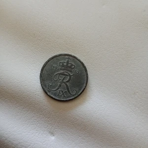 2 öre mynt från Danmark 1953 - Säljer ett danskt 2 öre mynt från 1953. Myntet är runt och i metall med texten '2 ØRE DANMARK' på ena sidan och kunglig krona samt monogram på andra sidan. Perfekt för samlare av nordiska mynt eller historiska föremål.