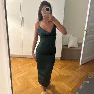 Mörkgrön satinklänning med smala axelband - Säljer en superfin mörkgrön satin klänning! Klänningen har gått sönder i slitsen men de är ihopsytt och är något som jag iallafall inte tänker på🩷