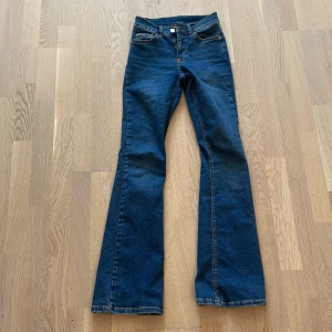 Blå bootcut jeans från Gina Tricot - Säljer ett par klassiska blå bootcut jeans från Gina Tricot, modell 'perfect jeans'. Jeansen har hög midja, fem fickor och stängs med dragkedja och knapp. Perfekta för dig som gillar en tidlös och snygg look.