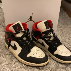 Nike Air Jordans svart, vit och röd - Säljer ett par klassiska Nike Air Jordans i svart, vitt och rött. Skorna har högt skaft, snörning och den ikoniska swoosh-loggan på sidan. Perfekta för dig som gillar streetwear och sneakers med retrostil.