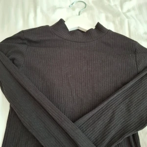 Svart ribbad långärmad tröja från H&M - Svart långärmad tröja från H&M med ribbad struktur och hög hals. Enkel och stilren modell som passar perfekt till många olika outfits. Mjuk och skön att ha på sig.