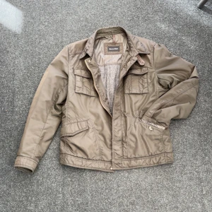 Olivgrön jacka från Massimo Dutti - Säljer en mörk gröna jacka från Massimo Dutti. Jackan är i mycket bra skick men har en liten defekt (sista bilden) men inget som påverkar skicket i stort. Den är fodrad med grått tyg på insidan och ger av en mycket klassisk och stilren look. 