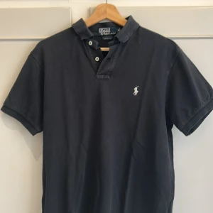  pikétröja från Polo Ralph Lauren - Klassisk svart pikétröja från Polo Ralph Lauren med vit broderad logga på bröstet. Tröjan har korta armar. väldigt fin piké använd lite men ändå bra skick, perfekt nu till sommaren