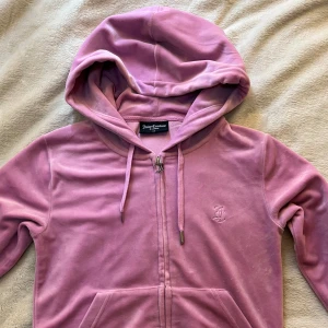 Rosa velour hoodie från Juicy Couture ÄKTA  - Mysig rosa hoodie i velour från Juicy Couture med dragkedja och huva. Klassisk logga på bröstet och snygg J-detalj på dragkedjan. Perfekt för en avslappnad och trendig look.