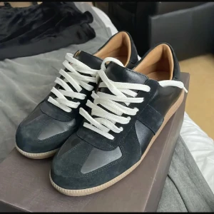 Svarta sneakers från Skolyx med vita snören - Stilrena svarta sneakers från Skolyx med vita snören och beige yttersula. Skorna har rund tå och är tillverkade i en kombination av skinn och mocka. Perfekta för en clean och klassisk look.