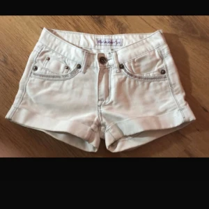 Low waist vita jeansshorts med fickor - Snygga low-waist vita jeansshorts.  Shortsen har silverfärgade nitar och knapp, samt dekorativa sömmar på bakfickorna.