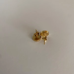 Guldpläterade runda örhängen - Säljer ett par stilrena, runda örhängen i guldpläterad metall. Framsidan har en glittrig, texturerad yta som ger extra lyster. Perfekta för dig som gillar minimalistiska smycken med en touch av elegans.