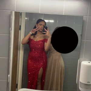 Röd glittrig långklänning med slit - Säljer min röda glittrig långklänning med en djup slits framtill som jag hade på min bal. Klänningen har figurnära passform och är perfekt för bal, fest och bröllop. Materialet är glittrigt och skimrande, vilket ger en lyxig känsla. Den är använd endast en kväll.