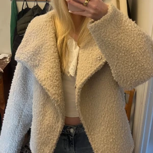 Beige teddyjacka med stor krage - Säljer en beige teddyjacka med stor, bred krage och asymmetrisk knäppning. Jackan är mjuk och fluffig.