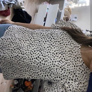 Vit blus med svarta prickar - Säljer en söt vit blus med svarta prickar och korta volangärmar. Blusen har en lös passform och rund halsringning. Perfekt att styla med jeans eller kjol för en trendig look.