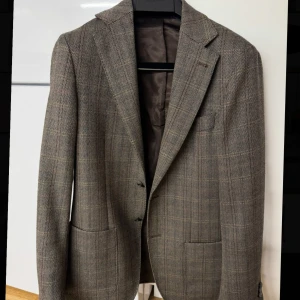 Stilren kavaj från Elson 1892 - stl 46 - Klassisk brunmelerad kavaj i fiskbensmönster från det klassiska märket Elson 1892. Storlek 46. Endast provad, i princip aldrig använd – i nyskick. Perfekt för både vardag och mer dressade tillfällen. Välsydd med fina detaljer och skön passform. Nypris 4999 kronor. 