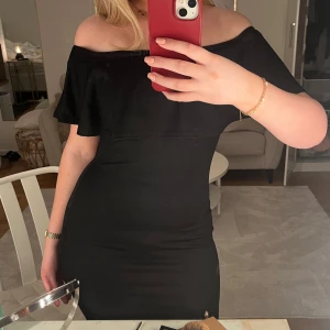 Svart offshoulder klänning med volang - Säljer en svart, tight offshoulder klänning från NLY One. Klänningen har volangdetalj upptill och är offshoulder 