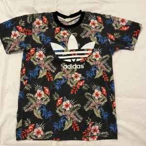 Blommig t-shirt från Adidas - Perfekt för dig som är lite osäker i dig själv. (Gärna under 184 annars blir den tajt)