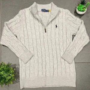 Ljusgrå stickad tröja med dragkedja från Polo Ralph Lauren - Säljer en ljusgrå stickad tröja från Polo Ralph Lauren med halv dragkedja och kabelstickat mönster. Tröjan har lång ärm, ribbade muddar och klassisk broderad logga på bröstet. Perfekt för lager-på-lager-stil.