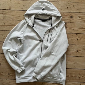 Sail Racing vit hoodie med dragkedja 170/Xs - Vit hoodie från Sail Racing med hel dragkedja och broderad logga på bröstet. Tröjan har huva, ribbade muddar och en extra dragkedjeficka framtill. Perfekt för en avslappnad stil.                       *Tröjan är lite trasig på fickansdragkedja och nån liten fläck på framsidan, märks inte så mycket av!(*se bild 4,5).                                                                   Priset kan diskuteras!