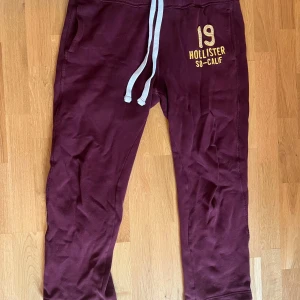 Mjukisbyxor från Hollister - Säljer ett par vinröda mjukisbyxor från Hollister med tryck och snörning i midjan. Byxorna är storlek L i herrmodell. Skicket är använt men bra
