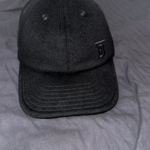 Svart keps från Burberry - Säljer en svart keps från Burberry med diskret broderad logga framtill. Kepsen har klassisk form och insidan har det ikoniska rutiga Burberry-mönstret. Perfekt accessoar för en stilren look. Kvitto från burberry finns på mejl. Köpt för 4300 kr.  