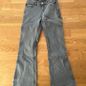 Jeans - Säljer ett par gråa bootcut jeans med klassisk femficksdesign och hällor för bälte. Jeansen har normal passform och är tillverkade i ett mjukt bomullsmaterial. Perfekta för dig som gillar en tidlös stil med lite utsvängda ben.