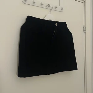 Svart manchesterkjol - Säljer en svart kortkjol i manchestertyg. Kjolen har klassisk passform med dragkedja och knapp framtill. Använd 2-3 gånger! (Katt finns i hemmet)