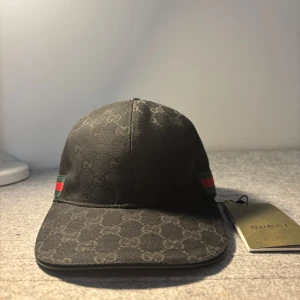 Svart keps från Gucci  - Skicka dm för video eller frågor. Snygg svart keps från Gucci med diskret GG-monogram över hela tyget och klassiska gröna och röda ränder på sidan. Justerbart spänne baktill i metall. Perfekt accessoar för en trendig look.