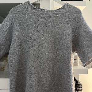 Grå stickad tröja från Vero Moda - Mysig grå stickad tröja från Vero Moda med korta ärmar och rund halsringning. Perfekt för lager-på-lager och enkel att matcha med olika outfits. Klassisk och stilren design. 