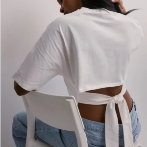 Vit topp med back tie  - Säljer en vit topp med korta ärmar och snygg knytning i ryggen. Toppen har en enkel och stilren design med rund halsringning och passar perfekt till typ allt. Använd en gång så den är fortfarande i nyskick