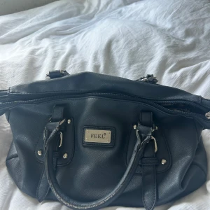 snygg handväska  - Säljer min markblåa handväska från märket feel. Väskan är använt och är lite sliten på några kanter men funkar super!