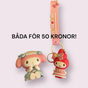 My Melody accessoarer/nyckelringar - Två söta My Melody accessoarer i pastellfärger. Ena är en figur med rosa och blå detaljer, andra är en röd My Melody med klänning och blomdetalj, fäst på en rosa rem med text. Perfekt att hänga på väskan eller använda som nyckelring.