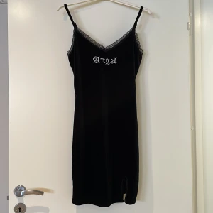 Svart sammetsklänning med spets - Svart sammetsklänning från SHEIN med spetsdetaljer. Klänningen har texten 'Angel' broderad framtill och en liten slits nertill. Perfekt för dig som gillar en stilren och edgy look. Använd endast en gång, stretchigt och behagligt tyg.