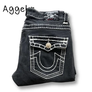 Svarta True Religion Jeans - Svarta jeansbyxor från True Religion med tydliga vita kontrastsömmar och dekorativa ficklock bak med knapp. Klassisk femficksmodell och raka ben. Perfekta för dig som vill sticka ut med detaljer. Strlk 31 men sitter som 30