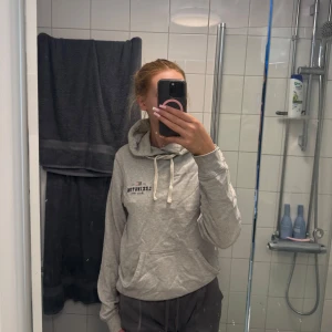 Grå hoodie från Lexington - Säljer en ljusgrå hoodie från Lexington med tryck på bröstet och klassisk känguruficka. Tröjan har huva med dragsko och långa ärmar. Perfekt för en avslappnad stil.