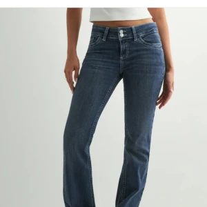 Blå snygga bootcut jeans från Nelly  - Snygga blå jeans med bootcut passform och dubbla knappar i midjan. Jeansen har klassiska fickor fram och bak med dekorativa sömmar på bakfickorna. Perfekta för en avslappnad och trendig look.