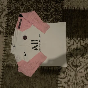 PSG långärmad fotbollströja från Nike - Säljer en långärmad PSG fotbollströja i vitt med rosa ärmar och svarta detaljer. Tröjan har klubbmärke på bröstet, Nike-logga och sponsortryck på både fram- och baksida. Materialet är lätt och andas, perfekt för träning eller match.