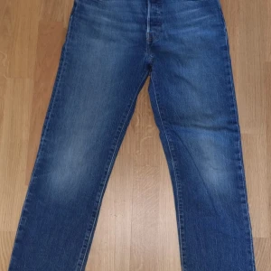 Levi's 501 blå jeans, W26 L28 - Klassiska blå Levi's 501 jeans med rak passform och femficksdesign. Jeansen har knappgylf och är tillverkade i slitstarkt denimtyg. Perfekta för dig som gillar tidlös stil och vill ha ett par jeans som funkar till det mesta.