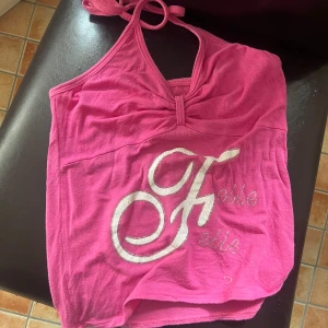 Rosa halterneck med tryck - Säljer en rosa halterneck top med knyt i nacken och ett stort vitt tryck framtill. Toppen har en lätt rynkad detalj vid bysten. Perfekt till sommaren .