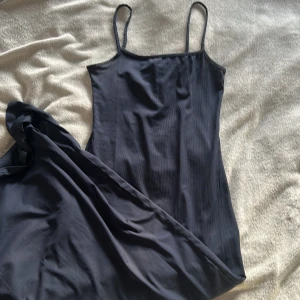 Mörkblå långklänning med smala axelband - En stilren mörkblå långklänning med smala axelband och rak passform. Klänningen har en minimalistisk design och är perfekt för dig som gillar enkelhet och elegans. Materialet känns mjukt och följsamt mot huden. Går ner till knäna på mig som är 168 cm.