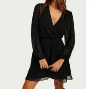 Svart chiffongklånning med långa ärmar - Säljer en svart omlottklänning med långa, transparenta ärmar och v-ringning. Klänningen har markerad midja och ett lätt, flödande tyg som ger en elegant siluett. Perfekt för dig som gillar stilrena och klassiska plagg.