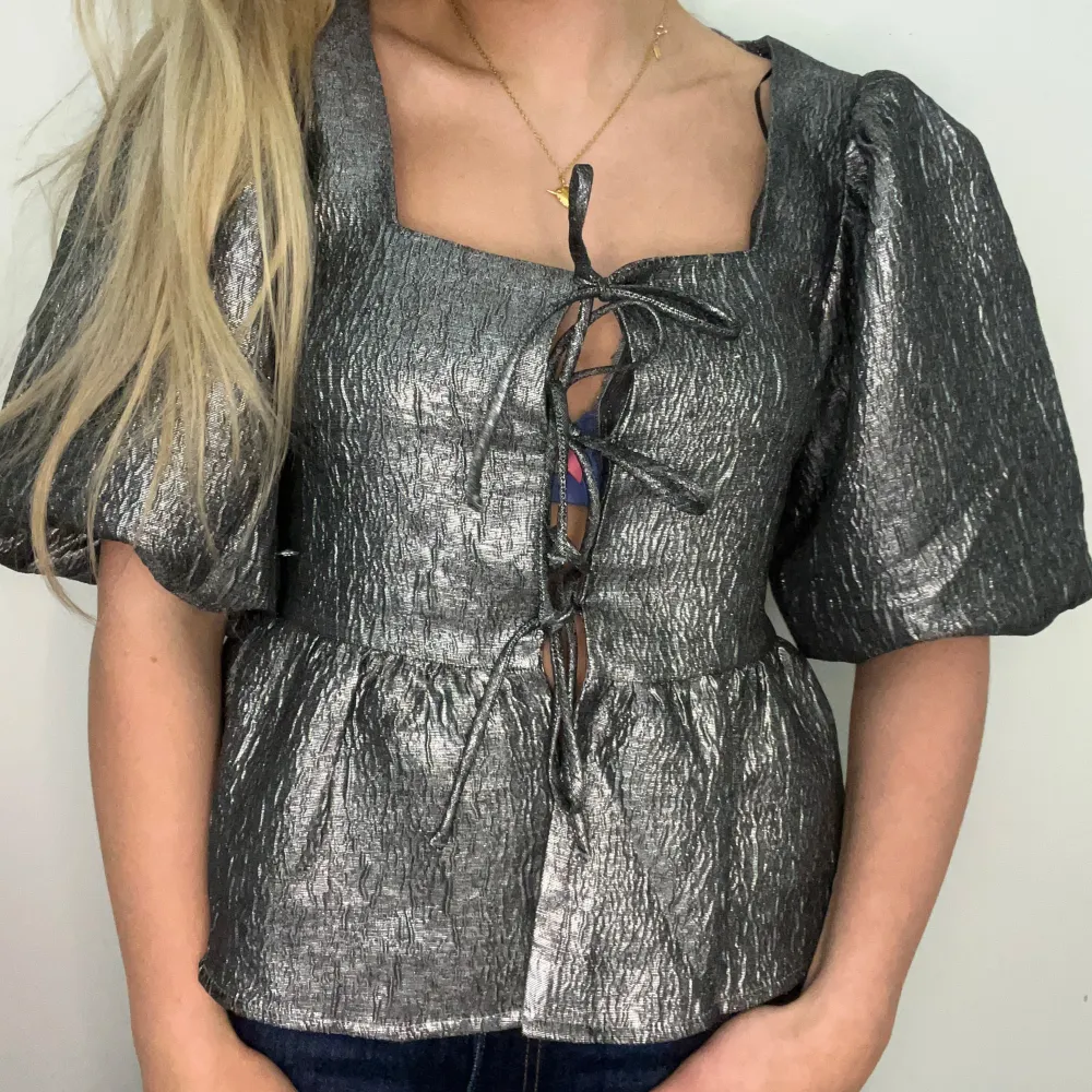 Snygg silverglittrig topp med puffiga kortärmar och knytning framtill. Perfekt för en festlig kväll!. Yläosat.