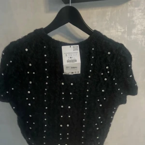 Svart tröja med pärlor - Snygg svart tröja dekorerad med pärlor som ger en elegant touch. Perfekt för att lyfta vilken outfit som helst. Kortärmad design som passar bra till både jeans och kjol.